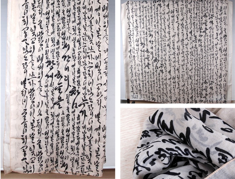 May include: A white fabric scarf with black calligraphy printed on it. The scarf is folded and draped over a surface. The calligraphy is in Korean.