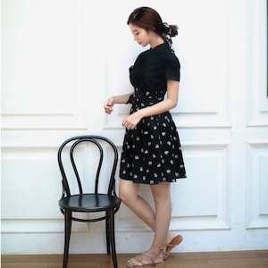 May include: A black dress with a white floral print and a short sleeve. The dress has a cinched waist and a flared skirt. The model is wearing brown sandals.