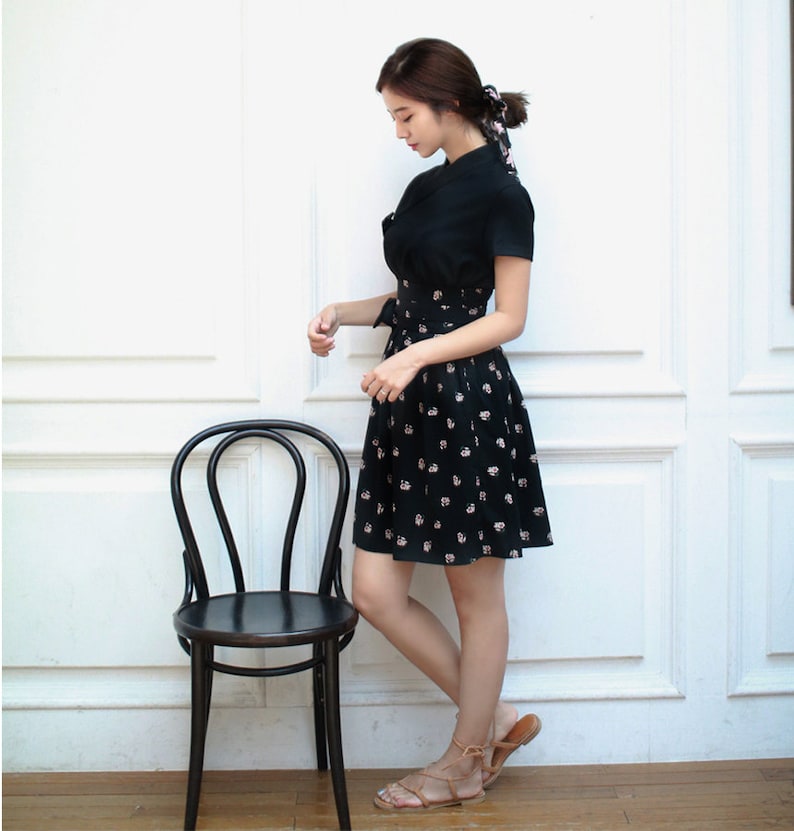 May include: A black dress with a white floral print and a short sleeve. The dress has a cinched waist and a flared skirt. The model is wearing brown sandals.