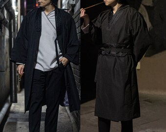 May include: Two people wearing black traditional Japanese robes with black sashes. The robes have a black trim around the collar and cuffs. The person on the left is holding a wooden stick.