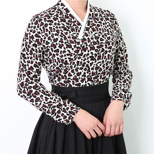 May include: A white blouse with a leopard print pattern and a black skirt. The blouse has a V-neck and long sleeves. The skirt is pleated and has a high waist.