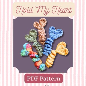 May include: Five crocheted heart-shaped ornaments with spiral stems in various colors including peach, blue, green, yellow, and a multi-colored yarn. The text Hold My Heart and PDF Pattern is displayed on a pink and white striped background.