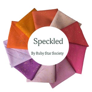 May include: A collection of fabric swatches arranged in a circular fan pattern, featuring various colors including orange, red, pink, and purple, all with a speckled pattern. A central white circle displays the text Speckled By Ruby Star Society.