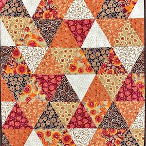May include: A quilt made of triangular fabric patches in shades of orange, brown, red, and white. The fabric features various patterns including floral, circles, and leaves.