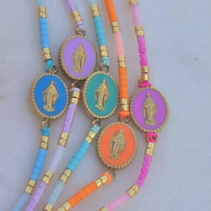 Op de afbeelding: Een verzameling kleurrijke armbanden met kralen. Elke armband heeft een goudkleurig medaillon met een religieuze figuur, omgeven door een gekleurde rand. De armbanden hebben verschillende kleuren, waaronder blauw, paars, oranje en roze.