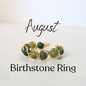 May include: A gold-toned wire ring featuring green gemstone beads. The ring is adjustable and has the word "August" and "Birthstone Ring" in black script.