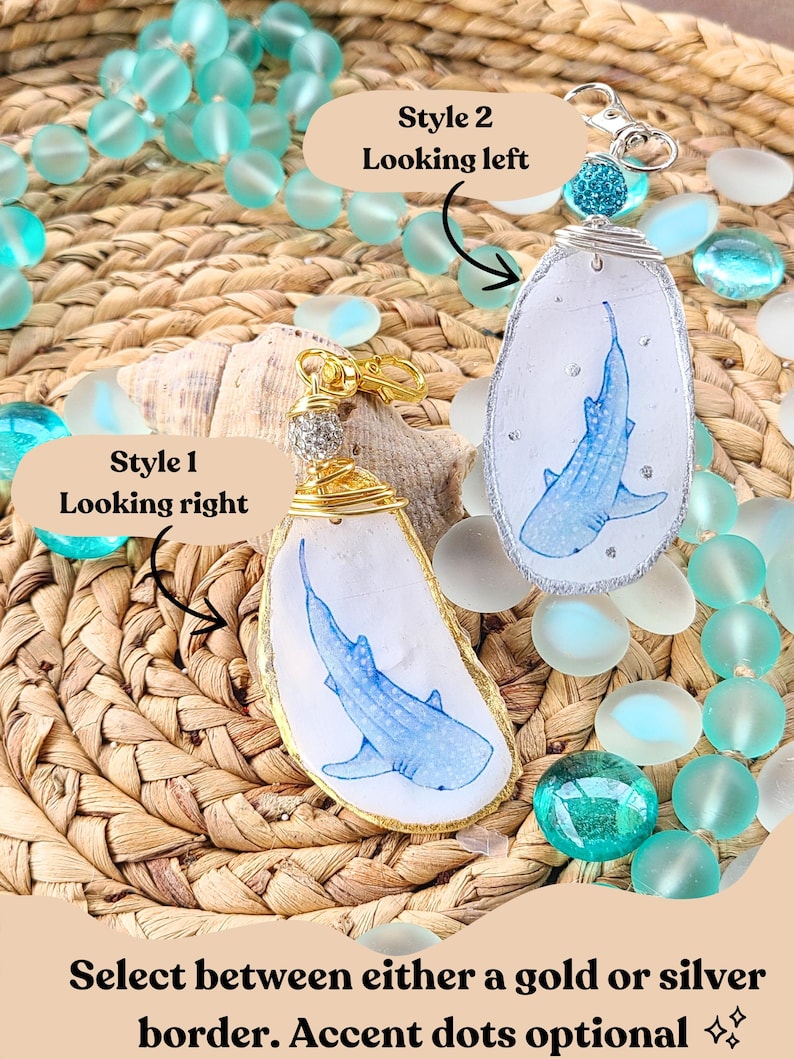 May include: Two handmade shark-themed keychains. One has a gold border, the other a silver border. Each features a blue shark illustration on a white background. The keychains are displayed with turquoise beads and a woven background.