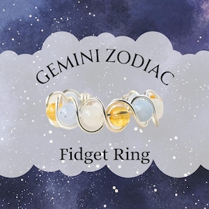 May include: A silver wire fidget ring with alternating yellow, white, and light blue beads. The ring is labeled "Gemini Zodiac Fidget Ring" against a starry background.