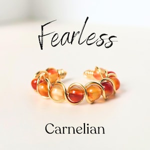 May include: A gold wire wrapped ring with carnelian beads. The ring is on a white background and the word "Fearless" is written above the ring. The word "Carnelian" is written below the ring.