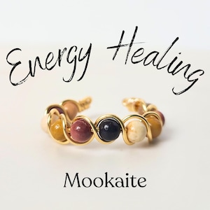 May include: Gold wire wrapped ring with a variety of colorful stones, including red, brown, yellow, white, and black. The ring is labeled "Mookaite" and "Energy Healing".