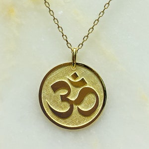 May include: A gold chain necklace with a round pendant featuring the Om symbol.