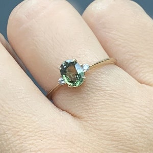 May include: A gold ring featuring a green oval gemstone and two smaller white gemstones set into the band.