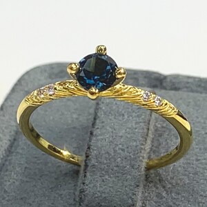 Könnte beinhalten: Ein goldener Ring mit einem blauen Edelstein und kleinen weißen Edelsteinen, die in die Band eingefasst sind.