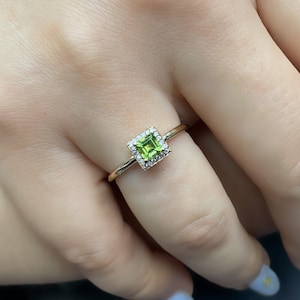 May include: A gold ring with a square green gemstone surrounded by smaller white gemstones.