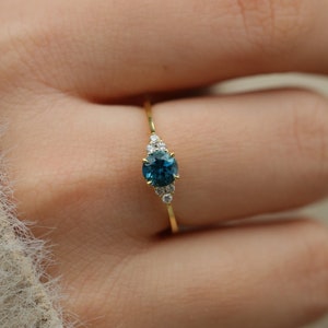 May include: A gold ring featuring a blue gemstone surrounded by smaller white gemstones.