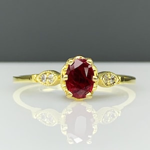 May include: A gold ring with a red ruby gemstone and two smaller diamonds on either side.