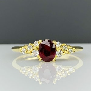 May include: A gold ring with a red oval gemstone surrounded by smaller white gemstones.