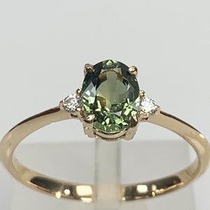 May include: A gold ring featuring a green oval gemstone with two smaller diamonds on either side.