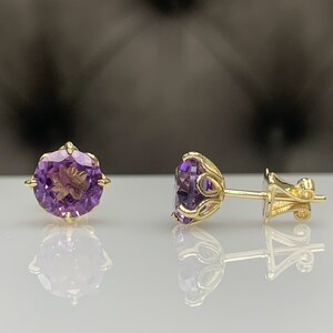Pu&ograve; includere: Un paio di orecchini d'oro con pietre preziose di ametista viola. Gli orecchini hanno un design delicato e decorato.