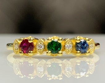 Op de afbeelding: Een gouden ring met vier edelstenen. De ring heeft een rode robijn, een groene smaragd, een blauwe saffier en twee witte diamanten.