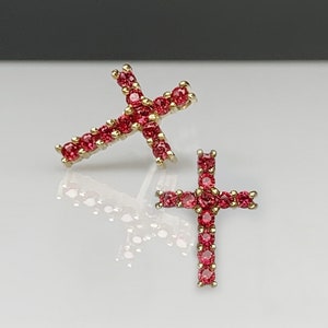 以下が含まれることがあります： 赤いキュービックジルコニアの石が付いた、金の十字架のイヤリングのペアです。