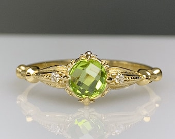 Puede incluir: Un anillo de oro con una piedra preciosa verde y pequeños diamantes. El anillo tiene un diseño delicado y adornado.