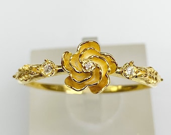 Può includere: Un anello d'oro con un delicato design floreale che presenta una rosa stilizzata con due piccoli diamanti sulla fascia.