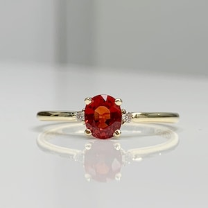 May include: A gold ring with a red gemstone and two smaller white gemstones.