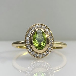 May include: A gold ring with a green oval gemstone surrounded by a halo of smaller diamonds.
