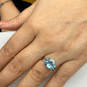 May include: A silver ring with a large oval-shaped blue topaz gemstone. The ring is set with smaller diamonds on the band.