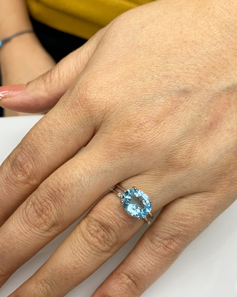 May include: A silver ring with a large oval-shaped blue topaz gemstone. The ring is set with smaller diamonds on the band.