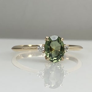 May include: A gold ring featuring a green oval gemstone with two smaller diamonds on either side.