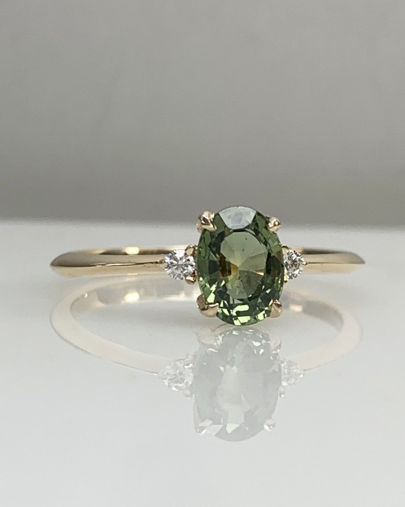 May include: A gold ring featuring a green oval gemstone with two smaller diamonds on either side.