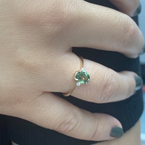 May include: A gold ring featuring a green oval gemstone and two smaller diamonds on the band.