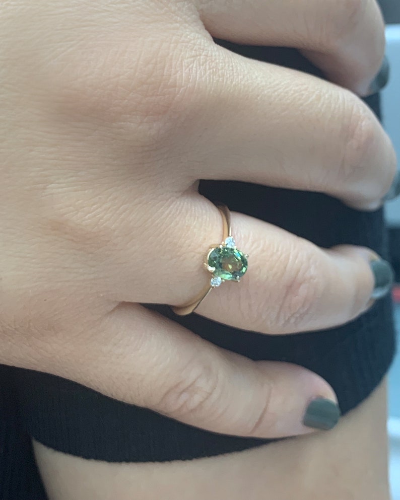 May include: A gold ring featuring a green oval gemstone and two smaller diamonds on the band.