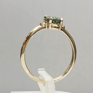May include: A gold ring featuring a green gemstone and two smaller diamonds set into the band.