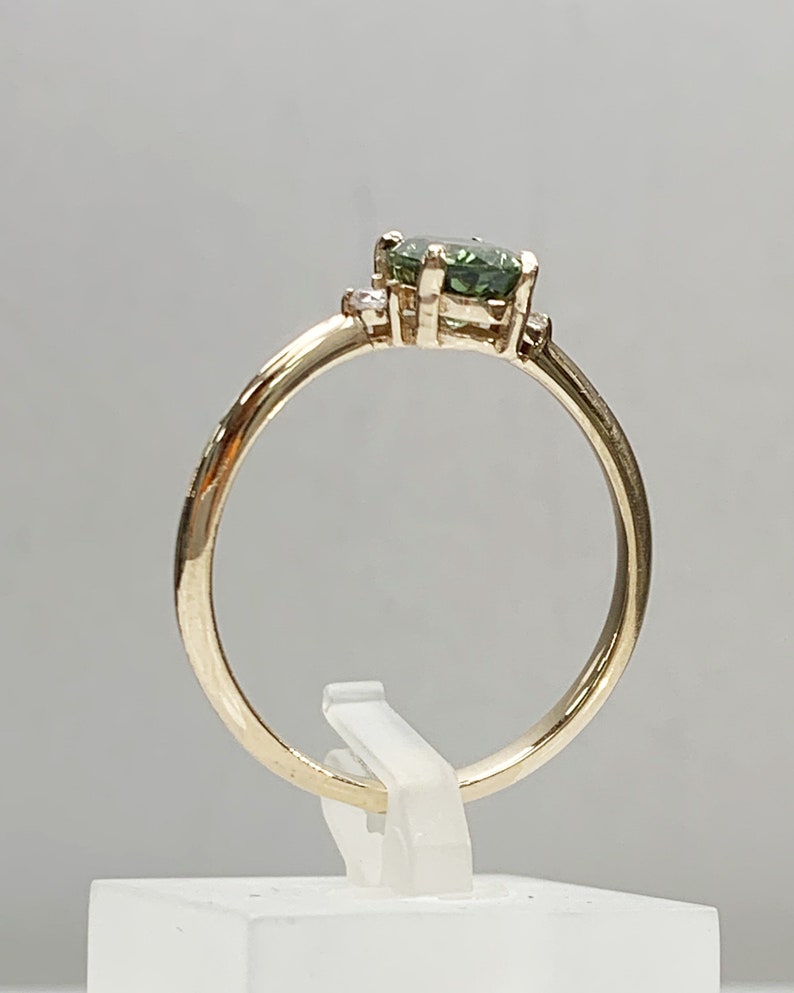 May include: A gold ring featuring a green gemstone and two smaller diamonds set into the band.