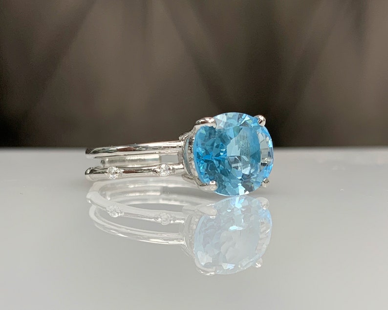 May include: A silver ring with a large oval-shaped blue topaz gemstone and smaller diamonds set in the band.
