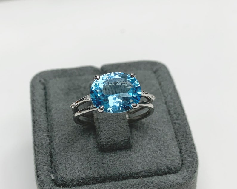 May include: A silver ring with a large oval-shaped blue topaz gemstone and smaller diamond accents.