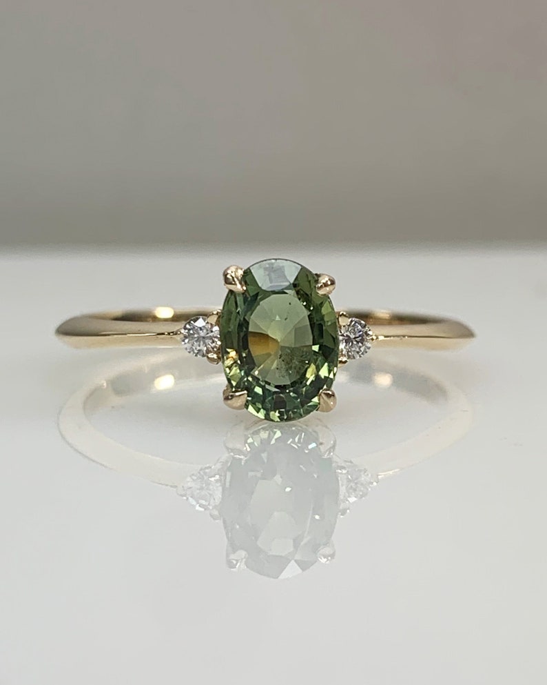 May include: A gold ring with a green oval gemstone and two smaller white gemstones on either side of the oval gemstone.