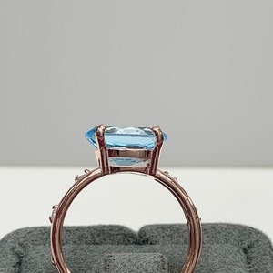 May include: A rose gold ring with a large, light blue gemstone and smaller clear gemstones around the band.