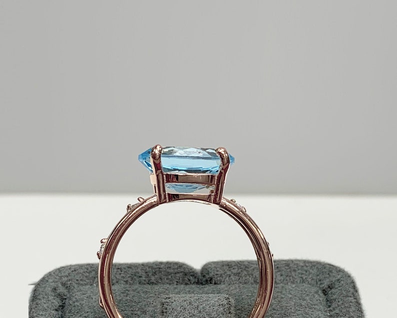 May include: A rose gold ring with a large, light blue gemstone and smaller clear gemstones around the band.