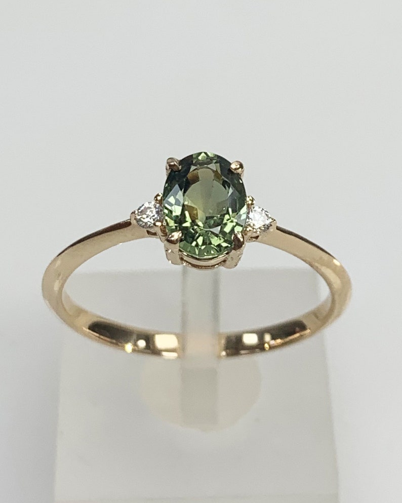 May include: A gold ring featuring a green oval gemstone with two smaller diamonds on either side.