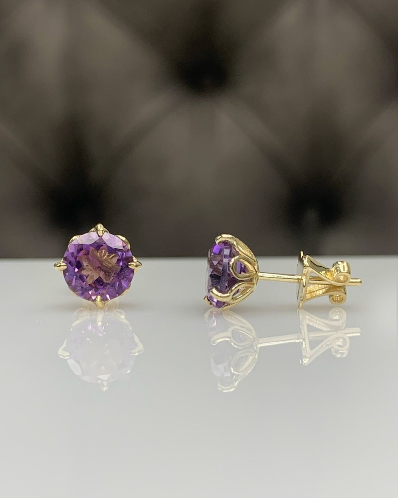 Pu&ograve; includere: Un paio di orecchini d'oro con pietre preziose di ametista viola. Gli orecchini hanno un design delicato e decorato.