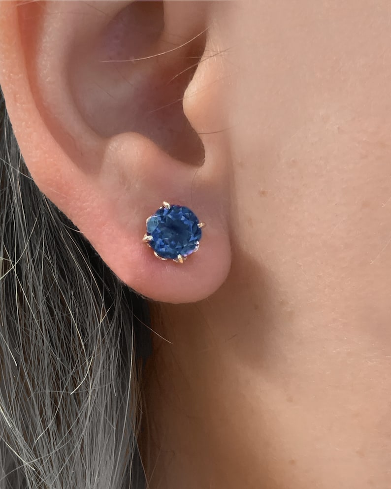 Pu&ograve; includere: Un paio di orecchini a perno d'oro con una pietra preziosa blu scuro al centro.