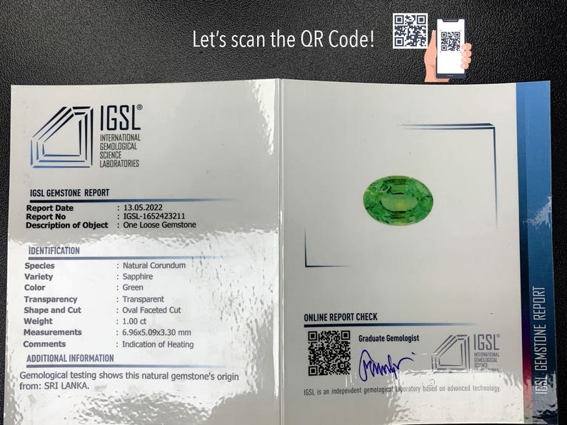 May include: IGSL Gemstone Report for a green sapphire gemstone. The report includes details such as the date, report number, species, variety, colour, transparency, shape and cut, weight, measurements, and comments. The report also includes a QR code for online verification.