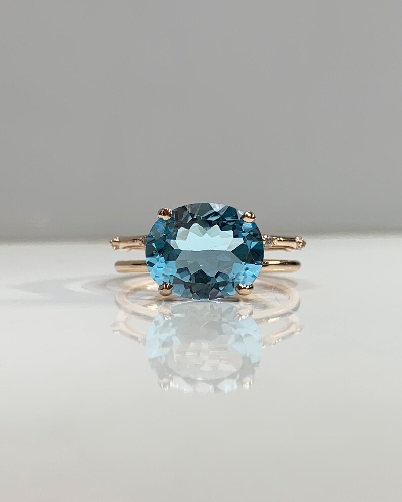 May include: A rose gold ring with a large oval-shaped blue topaz gemstone and smaller diamonds set in the band.