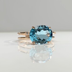 May include: A rose gold ring with a large oval-shaped blue topaz gemstone and smaller diamonds set in the band.