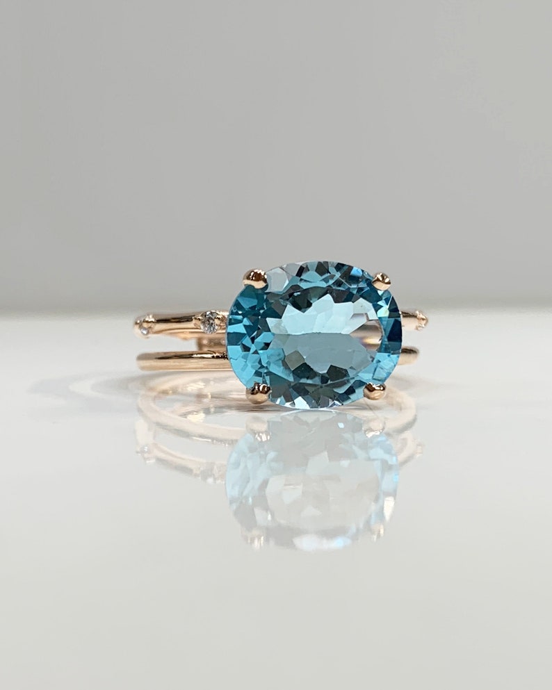 May include: A rose gold ring with a large oval-shaped blue topaz gemstone and smaller diamonds set in the band.