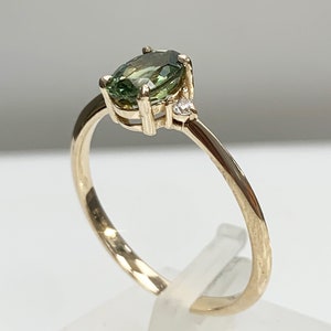 May include: A gold ring featuring a green oval gemstone and a smaller diamond accent.